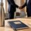 Garrafa e caderno personalizados sobre mesa de madeira com dois executivos apertando as mãos ao fundo, representando brindes para fornecedores e parceiros comerciais
