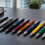 Canetas personalizadas coloridas organizadas sobre mesa de madeira escura, brinde corporativo